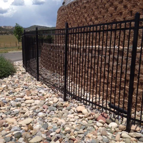 Black steel ornamental fence along a stone-bordered driveway with mountain backdrop